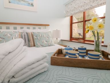 A bedroom with a bed with seagull patterned pillows a wooden tray with blue and white striped teapot cups and a vase with yellow flowers at Erin Cottage in Pelynt near Looe