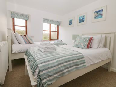 A bedroom with two single beds green striped blankets and bird patterned cushions at Erin Cottage in Pelynt near Looe