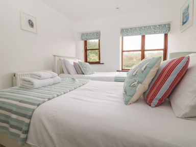 A bedroom with two single beds white walls striped throws and seagull patterned cushions at Erin Cottage in Pelynt near Looe