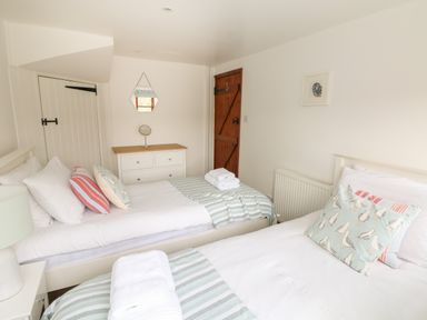 A bedroom with two single beds a white dresser and a wooden door at Erin Cottage in Pelynt near Looe