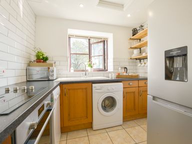 A kitchen with wooden cabinets a washing machine a microwave a refrigerator and a window at Erin Cottage in Pelynt near Looe