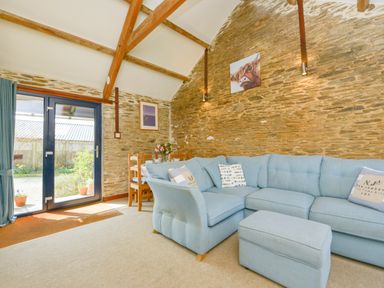 A living room with a blue sectional sofa a matching ottoman a wooden dining table with chairs and glass doors at Erin Cottage in Pelynt near Looe