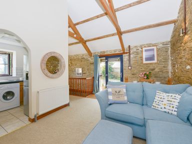 A living room with stone walls a blue sofa wooden beams and a kitchen visible through an archway at Erin Cottage in Pelynt near Looe