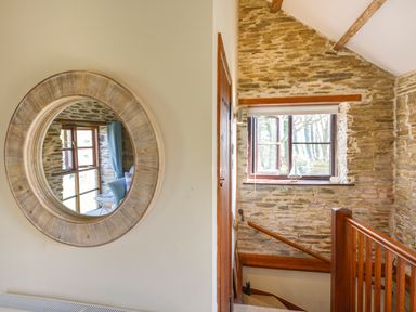 A staircase with wooden railing and a window with a small sailboat decoration on the sill at Erin Cottage in Pelynt near Looe