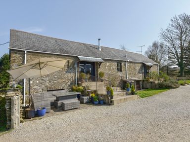 An outdoor seating area with an umbrella and stone steps leading to doors at a stone cottage at Erin Cottage in Pelynt near Looe