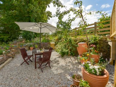 An outdoor patio with a table and chairs under an umbrella with potted plants and a wooden fence at Erin Cottage in Pelynt near Looe