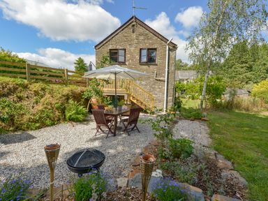 An outdoor patio area with a table and chairs under an umbrella and a stone house in the background at Erin Cottage in Pelynt near Looe