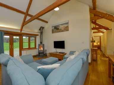 A living room with blue sofas a wood stove and wooden beams on the ceiling at Hook Cottage in Pelynt near Looe