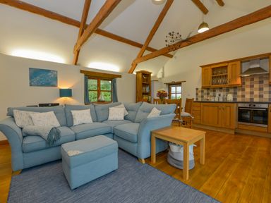 An open living room and kitchen with a blue sectional sofa wooden beams and a dining table at Hook Cottage in Pelynt near Looe