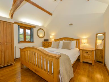 A bedroom with wooden bed frame bedside tables wardrobe and mirror at Hook Cottage in Pelynt near Looe