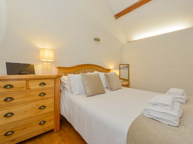 A bedroom with a double bed white and beige linens wooden furniture and bedside lamps at Hook Cottage in Pelynt near Looe