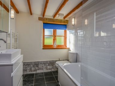 A bathroom with a sink, toilet, bathtub, window with blue blind, and exposed wooden ceiling beams at Hook Cottage in Pelynt near Looe