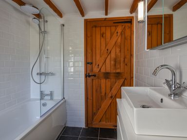 A bathroom with a bathtub shower combination a wooden door and a white sink at Hook Cottage in Pelynt near Looe