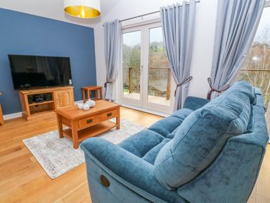 A living room with a blue sofa wooden coffee table and television at 1 Lake View in Lanreath