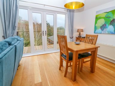 A dining area with wooden table and chairs next to glass doors with curtains and a blue sofa at 1 Lake View in Lanreath