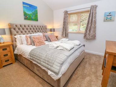 A bedroom with a bed with pillows and folded towels beside nightstands and a window at 1 Lake View in Lanreath