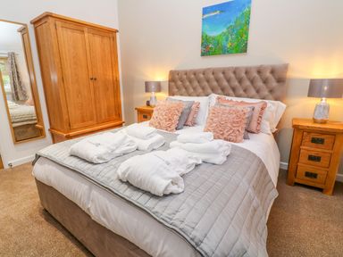 A bedroom with a double bed with cushions bedside tables lamps and a wooden wardrobe at 1 Lake View in Lanreath