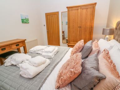 A bedroom with a wooden wardrobe a desk and a bed with decorative pillows and towels at 1 Lake View in Lanreath