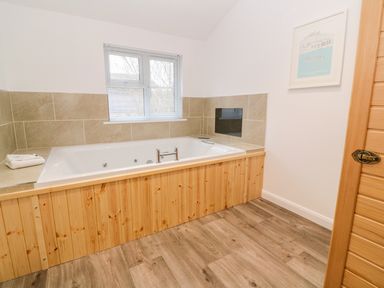 A bathroom with a bathtub surrounded by wooden panels and beige tiles at 1 Lake View in Lanreath