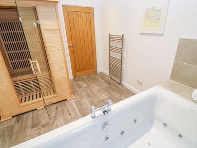 A bathroom with a bathtub wooden sauna door and a metal towel rack at 1 Lake View in Lanreath