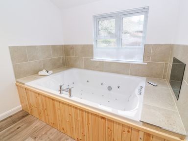 A bathroom with a large white jacuzzi tub surrounded by beige tiles and wooden paneling at 1 Lake View in Lanreath