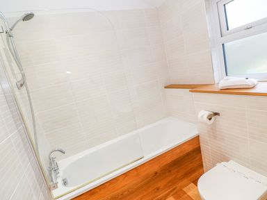 A bathroom with a bathtub and shower head a toilet and a window with a wooden shelf at 1 Lake View in Lanreath