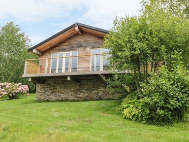 A wooden house with a stone base surrounded by greenery and trees at 1 Lake View in Lanreath