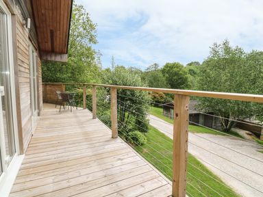 A wooden balcony with two chairs overlooking trees and a gravel path at 1 Lake View in Lanreath