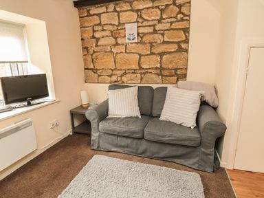 A sofa with two cushions in front of a stone wall with a small framed picture above it and a television on a window sill in a living room at Wren Cottage in Morpeth