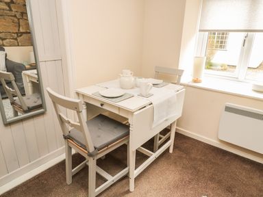 A small dining area with a white table set for two with plates cups and a teapot next to a window at Wren Cottage Morpeth