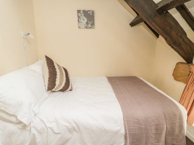 A bed with white sheets and a brown-striped pillow under a beam in a bedroom at Wren Cottage in Morpeth