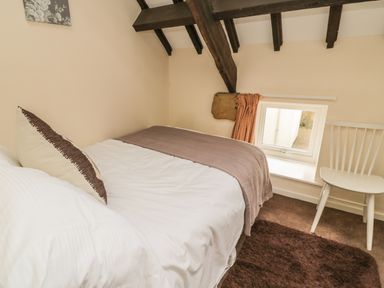 A small bedroom with a single bed pillow blanket and a white chair near a window at Wren Cottage in Morpeth
