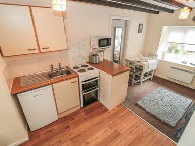 A kitchen area with a sink stove and microwave next to a dining table and window at Wren Cottage Morpeth
