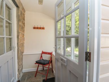 A small entryway with a red chair with a cushion stone wall and a white door at Wren Cottage in Morpeth