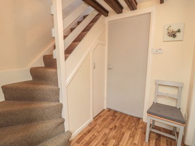 A staircase with brown carpet next to a closed gray door and a gray chair on wooden floor at Heron Cottage in Morpeth