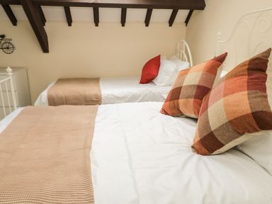 A bedroom with two single beds with checkered and red pillows and beige blankets under a ceiling with wooden beams at Heron Cottage in Morpeth