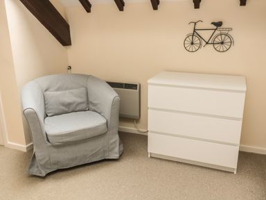 A grey armchair and a white three-drawer chest under a bicycle wall decoration in a room at Heron Cottage Morpeth