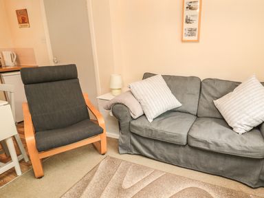 A grey armchair and a grey sofa with cushions in a living room at Heron Cottage in Morpeth