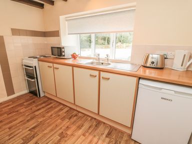 A kitchen with wooden floor cabinets a microwave oven a toaster a kettle a sink and a small refrigerator at Heron Cottage in Morpeth