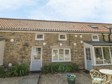 Stone cottage exterior with two doors two windows plants in front and outdoor table and chairs at Heron Cottage in Morpeth