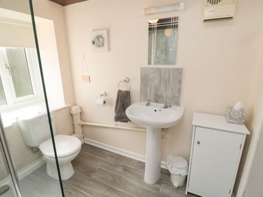 A bathroom with a toilet, pedestal sink, mirror, storage cabinet, and a window at Heron Cottage in Morpeth