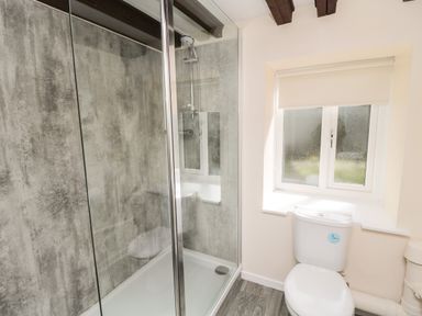 A bathroom with a shower enclosure, toilet, window with a blind, and a wooden floor at Heron Cottage in Morpeth