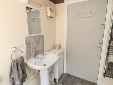 A bathroom sink with two taps beside a cabinet and a closed door at Heron Cottage in Morpeth