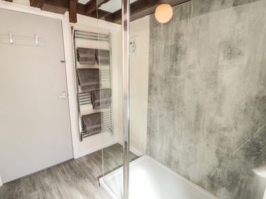 A bathroom with glass shower enclosure gray towels on a chrome towel rack and a textured gray wall at Heron Cottage in Morpeth