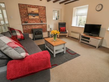 A living room with a sofa and cushions a coffee table and tv at Magpie Cottage in Morpeth