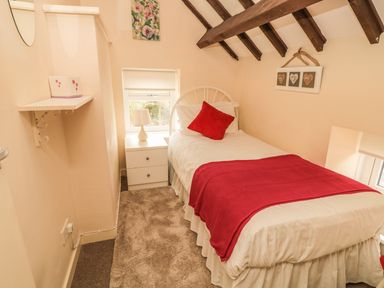 A small bedroom with a single bed with red pillow and blanket a bedside table with lamp and exposed wooden beams at Magpie Cottage in Morpeth