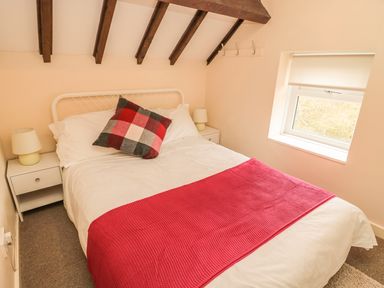 A bedroom with a double bed red blanket checkered pillow bedside tables with lamps and a window at Magpie Cottage in Morpeth