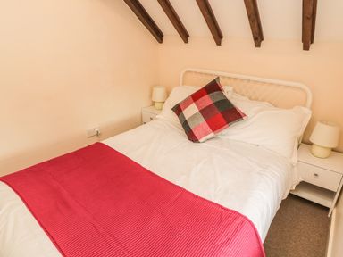 A bedroom with a bed with a red blanket and a checkered pillow with bedside tables and lamps at Magpie Cottage in Morpeth