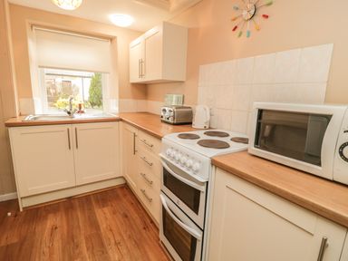 A kitchen with a white stove, microwave, toaster, kettle, cabinets, window, and wooden floor at Magpie Cottage in Morpeth