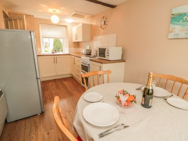 A kitchen with dining table set with plates and a bottle and cabinets with appliances at Magpie Cottage in Morpeth
